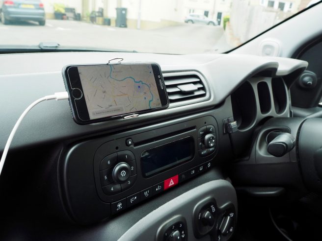 An image of a mobile phone being held in place on a car's air vents with a bulldog clip.