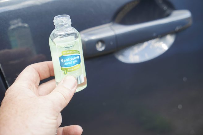 An image of a bottle of hand sanitiser near a car door.